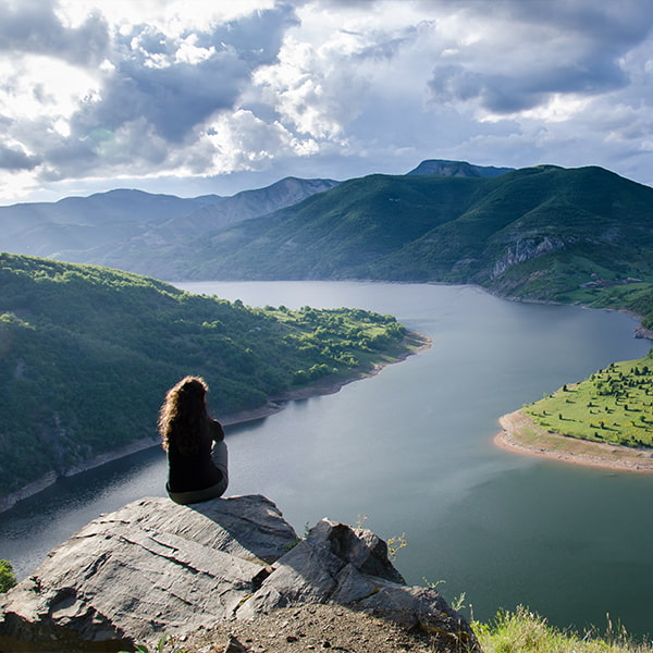 Woman sat on the top of a mountain looking across a lake